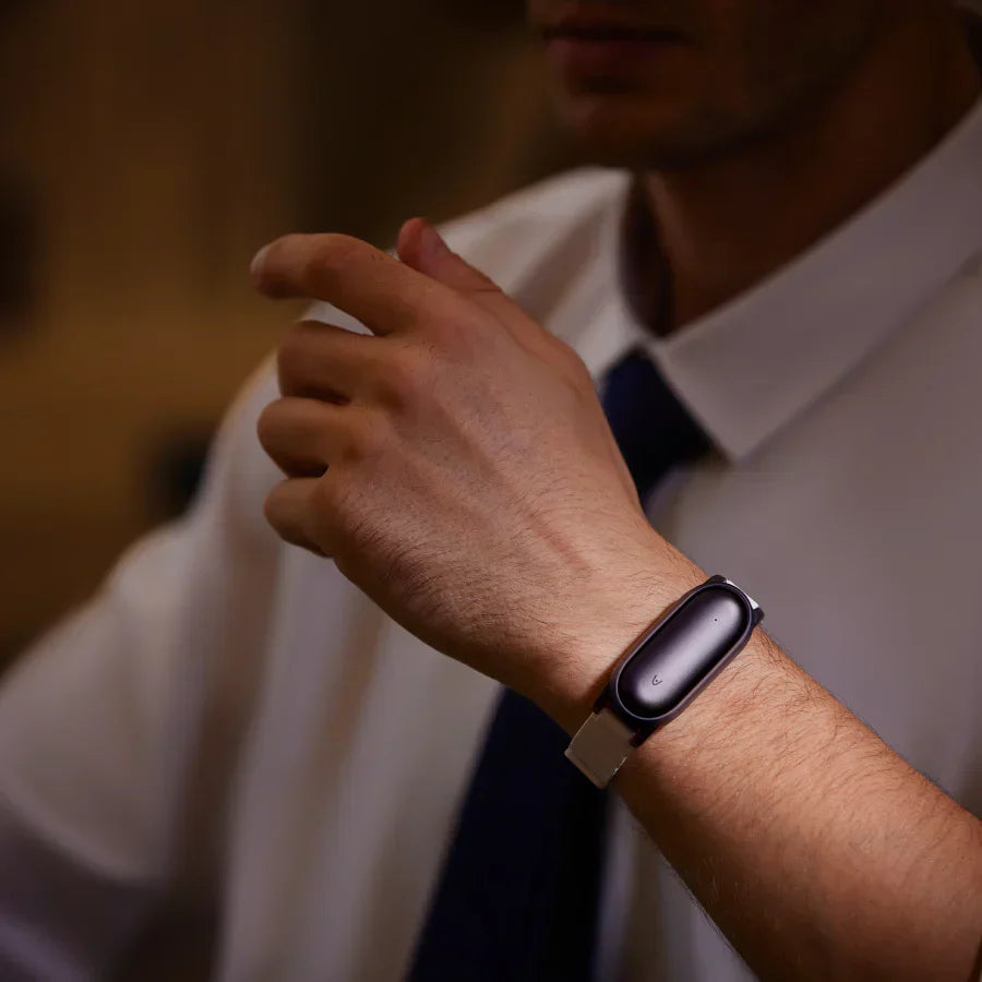 A professional in a white shirt and tie wears a dark purple Plaud NotePin on a silver wristband.