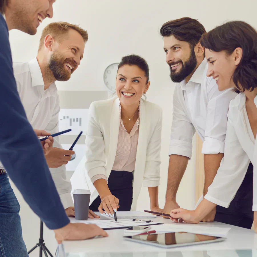 Five smiling professionals collaborate around a table during a meeting with a silver Plaud Note Pro attached to a smartphone.